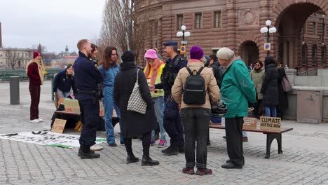 protesters outside swedish parliament with signs for climate justice talk to police officer