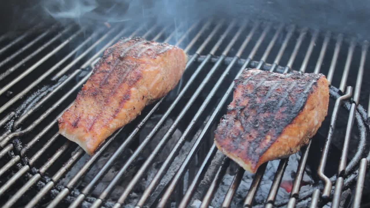 Fumo che si alza da filetti di salmone carbonizzati che grigliano su un barbecue a carbone da esterno