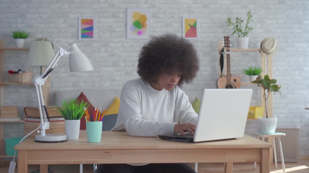 beautiful african american woman with an afro hairstyle uses a laptop at home
