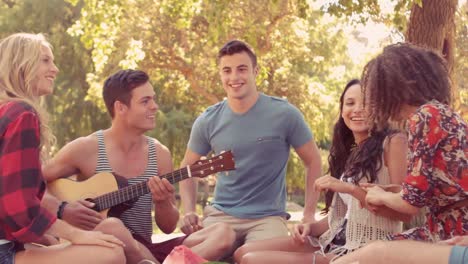 Hombre-Hipster-Tocando-La-Guitarra-En-El-Parque-Con-Sus-Amigos