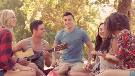 hombre hipster tocando la guitarra en el parque con sus amigos