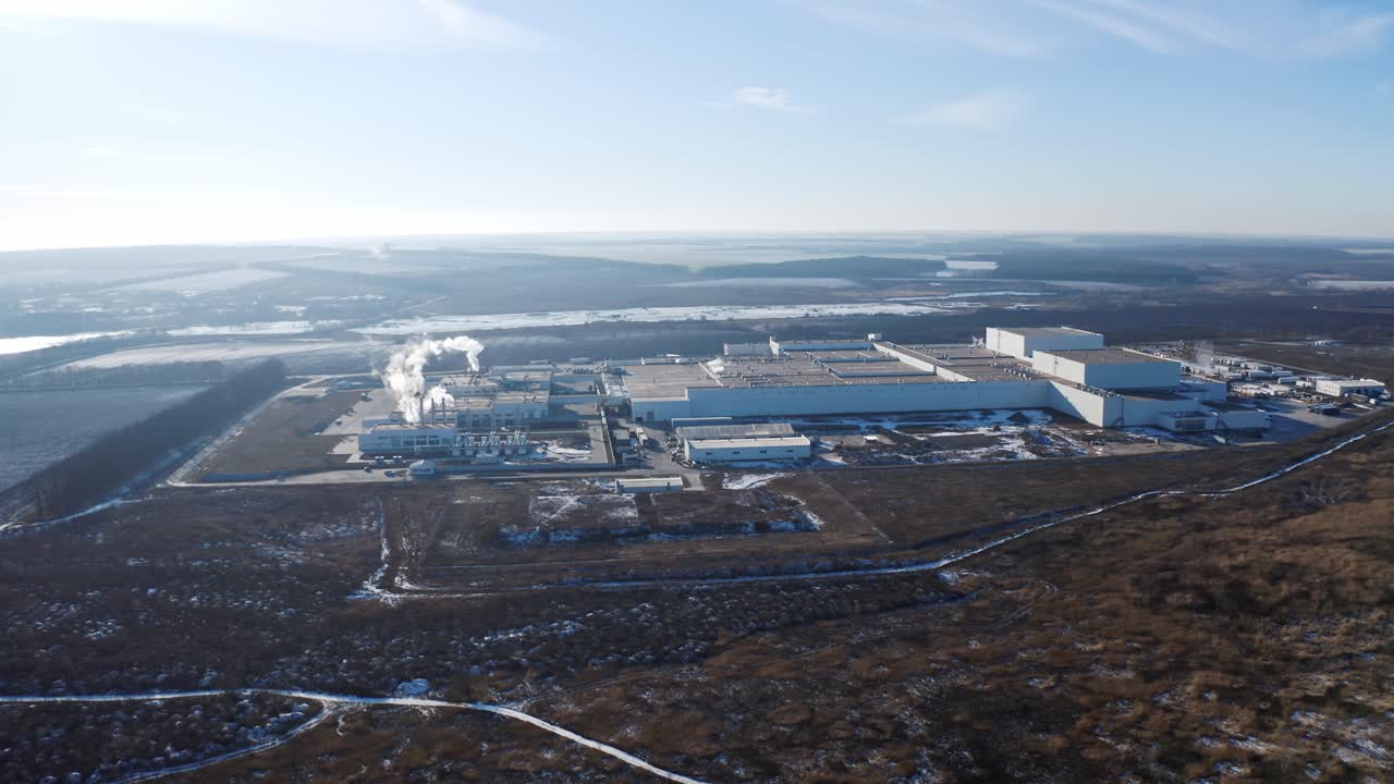 Big territory of industrial factory surrounded by nature. View from above on the roofs of a modern plant in the countryside in winter. Aerial view.