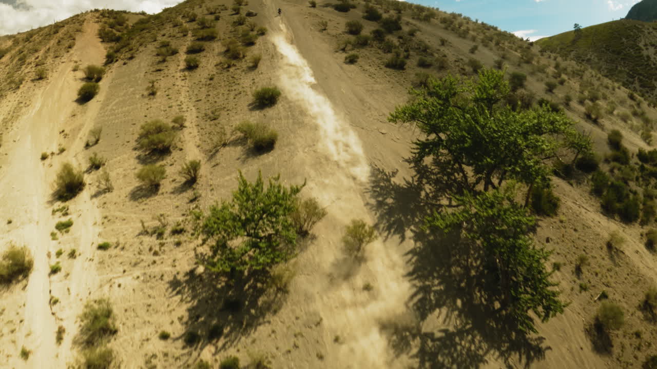 un sendero curvo de polvo sigue a un motociclista en colinas arbustos fpv. un motociclista viaja hasta el pico de la montaña durante las carreras de motocross. un majestuoso paisaje aéreo