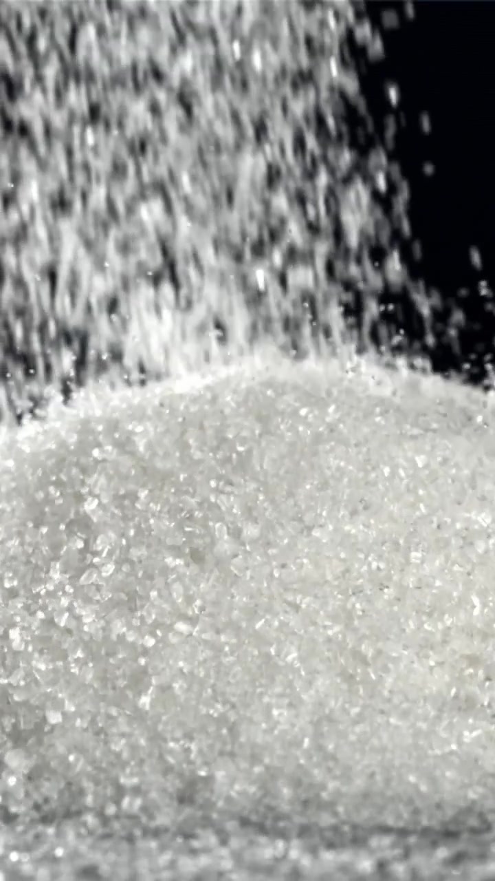 Zucchero semolato bianco che cade su un mucchio su sfondo nero