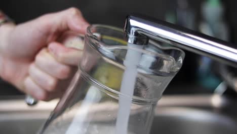 glass jug being filled with water from kitchen tap