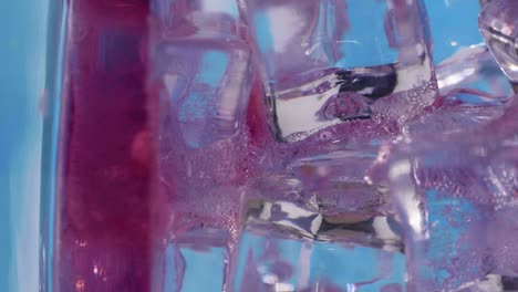 disparo estático en cámara lenta de una bebida de frutas vertida en un vaso con cubitos de hielo, fondo azul, vertical
