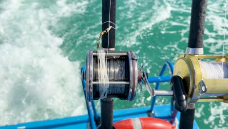 fishing rods and reels on a boat in chalong bay, phuket, with ocean waves and bright daylight