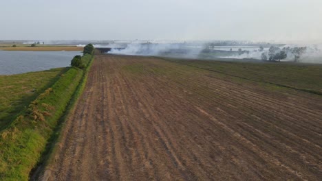 Descending-aerial-footage-showing-a-tilled-farmland-and-smoking-rising-making-pollution-in-Pak-Pli,-Nakhon-Nayok,-Thailand