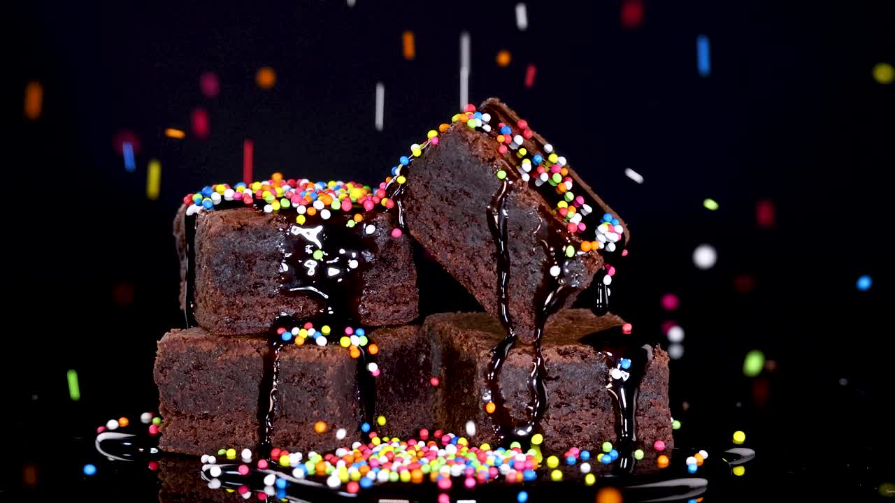 Stacked chocolate brownies with chocolate sauce and rainbow sprinkles, slow motion, dramatic lighting