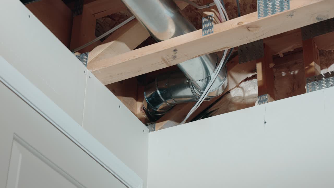 A Long 4K Zoom Shot of the Corner in an Unfinished Basement In a Newly Constructed Built Home Showing Metal HVAC Tubes Two by Four Lumber Drywall Wires Pipes and Insulation Above a White Door