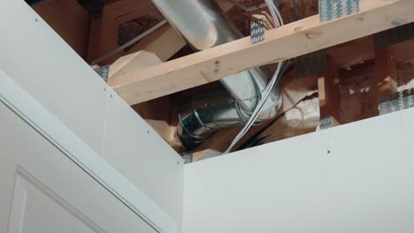 a long 4k zoom shot of the corner in an unfinished basement in a newly constructed built home showing metal hvac tubes two by four lumber drywall wires pipes and insulation above a white door