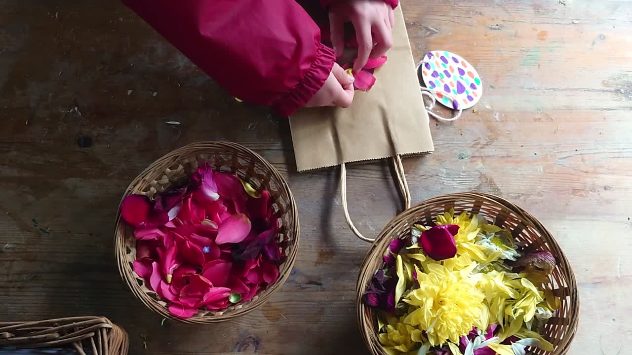 A creative hands-on moment as a person carefully arranges fresh rose and chrysanthemum petals into a rustic paper gift bag. Ideal for DIY enthusiasts and nature-inspired packaging concepts.