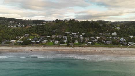 onetangi beach, sandy shore, people, coastal road, and hillside houses, waiheke island, new zealand. aerial drone lateral view
