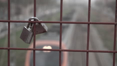 two love locks on a fence of a bridge over train tracks as a train passes underneath