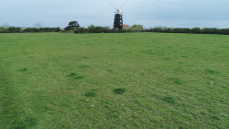 Rising-Aerial-Drone-Shot-Over-Grass-Field-Towards-Old-Windmill-Revealing-Salt-Marsh-Behind-in-Burnham-Overy-Staithe-North-Norfolk-UK