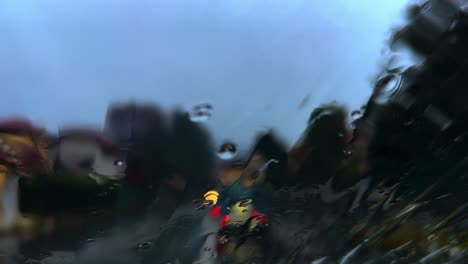 mal tiempo con lluvia y gotas de lluvia heladas deslizándose sobre el parabrisas húmedo con luces borrosas de tráfico de automóviles en segundo plano
