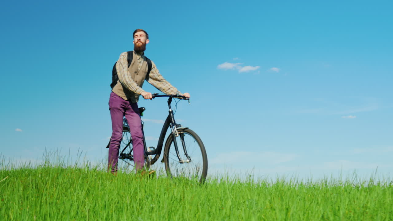 젊은 힙스터 남자가 녹색 초원을 통해 자전거를 운전합니다.
