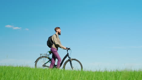 a young hipster man drives a bicycle through a green meadow