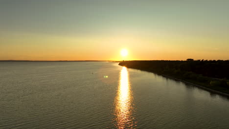 aerial view of a calm body of water with the sun setting in the horizon, casting a golden reflection on the water - kuźnica, poland