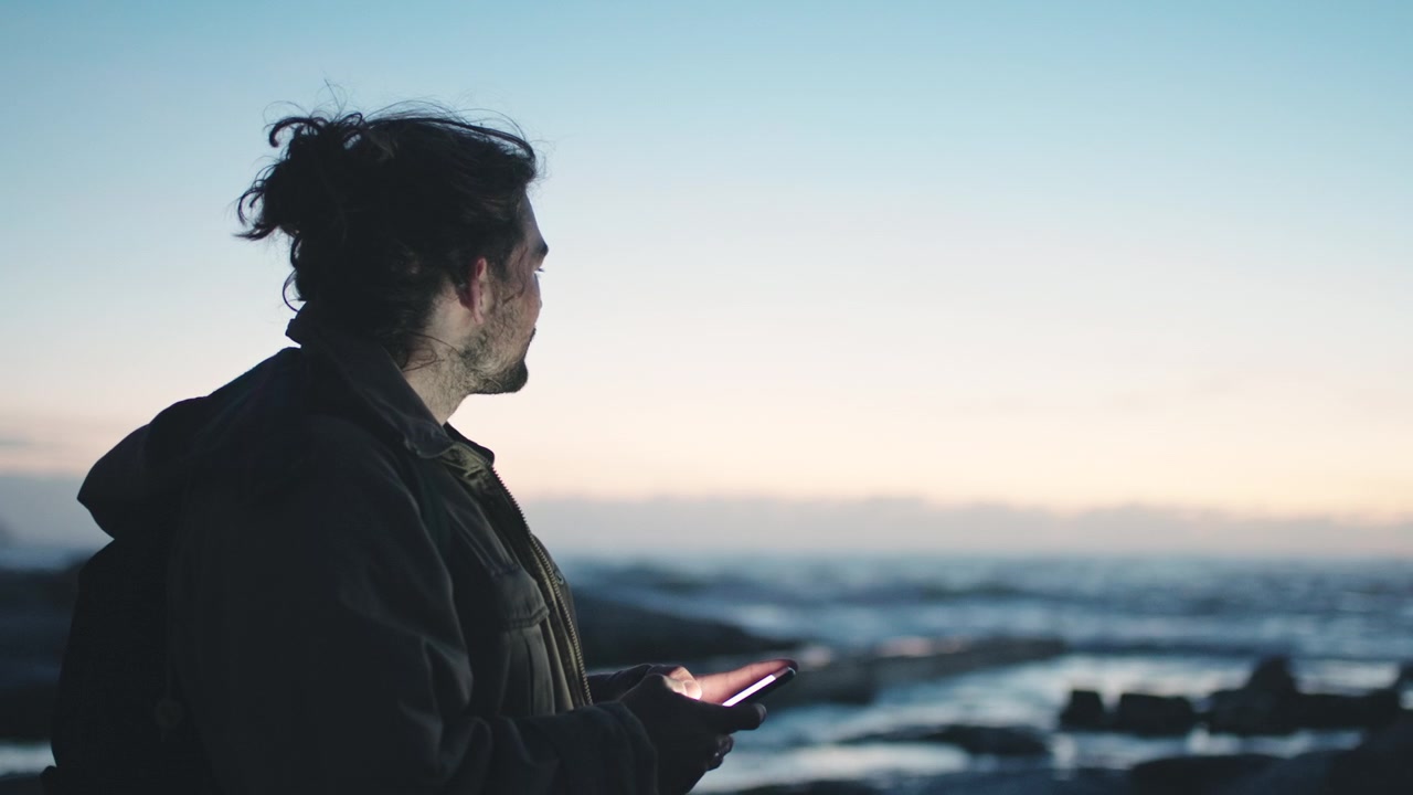 Ragazzo che usa lo smartphone in riva all'oceano al tramonto