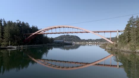 Passing-under-the-rainbow-bridge-in-LaConner,-Washington,-amazing-reflections-in-the-harbor,-aerial