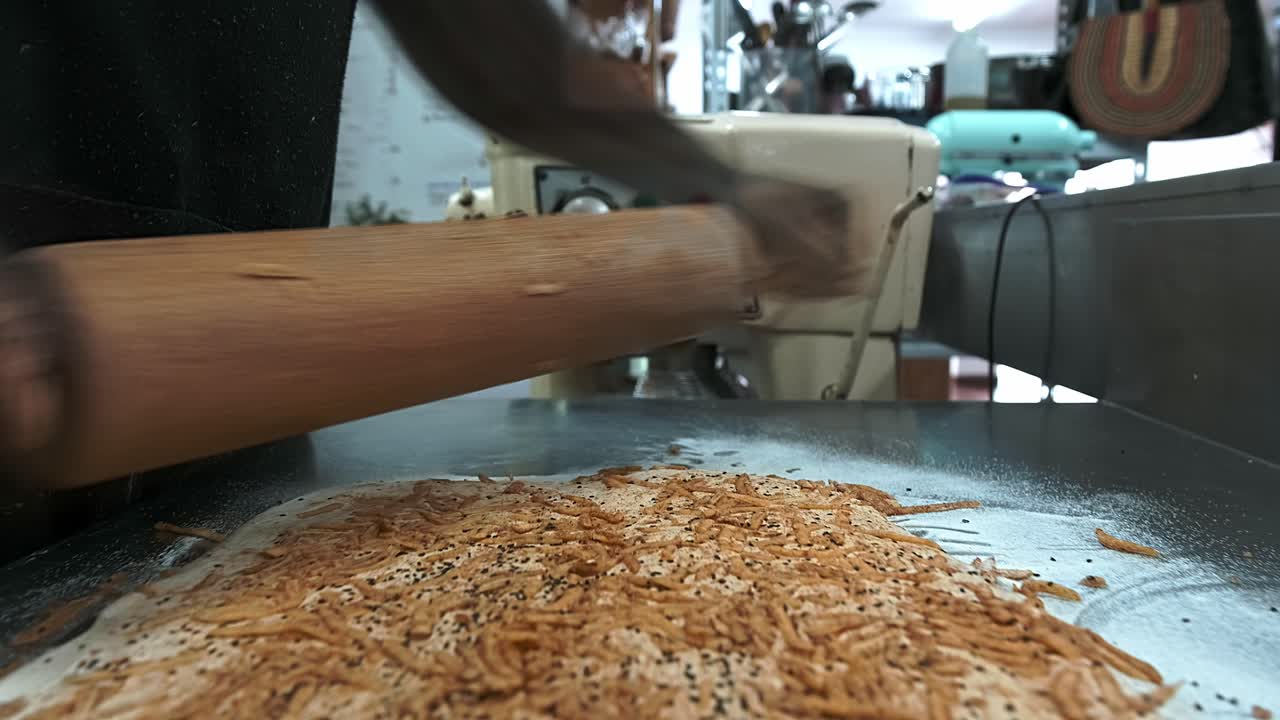 Baker rolls out a piece of dough with cheese to make bread sticks