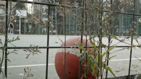 Nahaufnahme-Eines-Einsamen-Roten-Balls-Und-Teenager-Spielen-Basketball-Auf-Einem-Beton-Basketballplatz-In-Zeitlupe