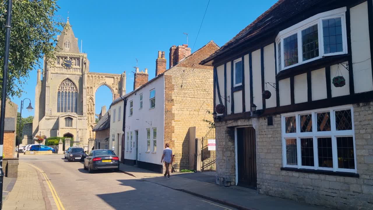 A lone man walking through Crowland village toward the historic Abbey ruins in the UK on a sunny summer day, capturing local life and heritage architecture