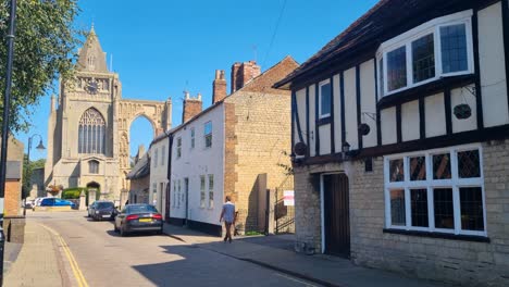 a lone man walking through crowland village toward the historic abbey ruins in the uk on a sunny summer day, capturing local life and heritage architecture