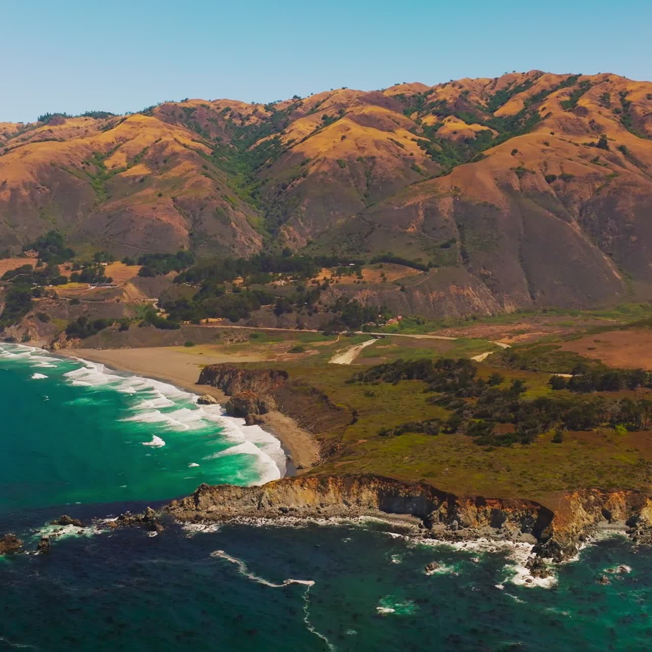 Amazingly beautiful shades of blue in the ocean near rocky shore. Brown orange mountains with rounded tops at backdrop