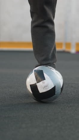 vista de la pierna de un atleta que demuestra giros precisos del tobillo con las piernas izquierda y derecha, equilibrando hábilmente la pelota de fútbol en una arena deportiva con poste de portería y pared pintada