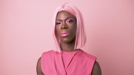 transgender person in pink dress making up with pink lipstick on pink background