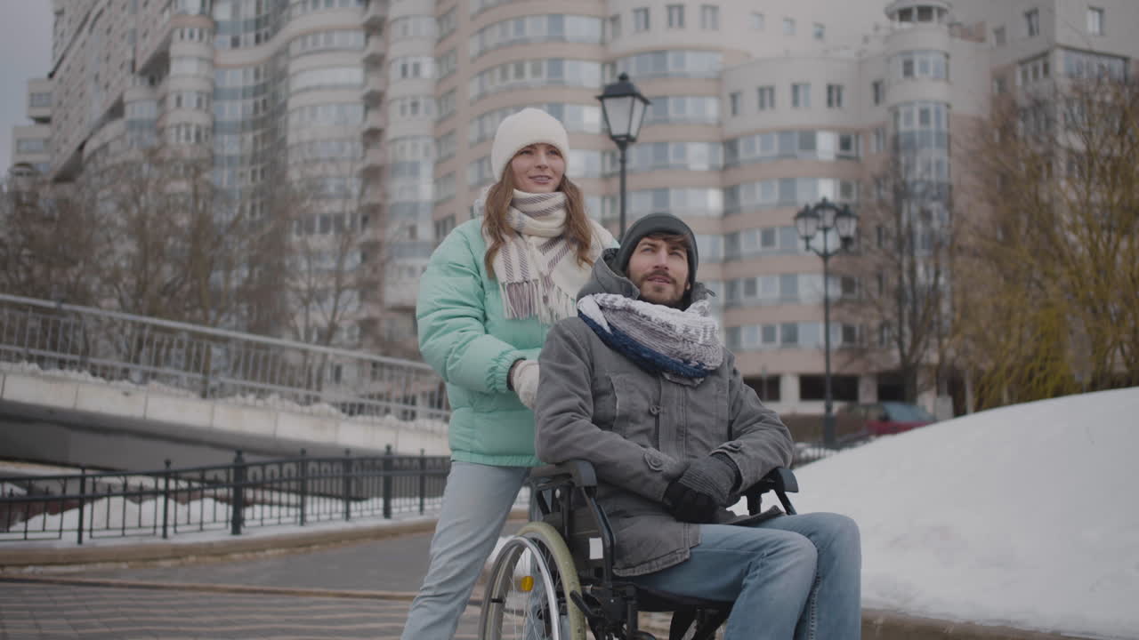 Funny Caucasian woman and disabled man in wheelchair talking and having fun together in the city in winter