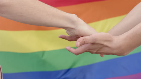 midsection of diverse gay male couple holding hands over rainbow lgbt flag, slow motion