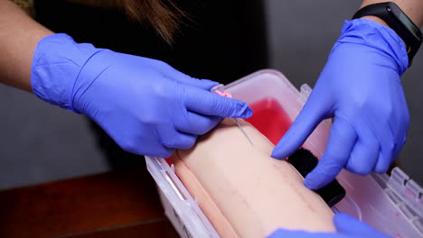 surgeon student trains to inserting needle for catheter on medical dummy. hands in blue latex gloves.