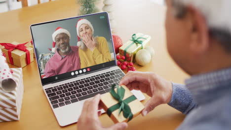 biracial man with gift having laptop video call with happy diverse couple