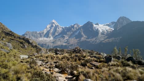 a winding rocky pathway carves through dramatic, rugged terrain surrounded by alpine grass and towering peaks along peru's iconic santa cruz trek in the cordillera blanca - aerial flyover