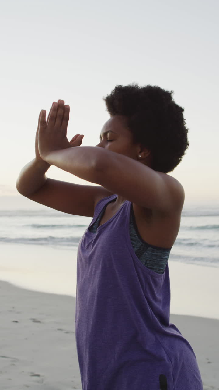 Video verticale di una donna afroamericana rilassata che pratica yoga in spiaggia