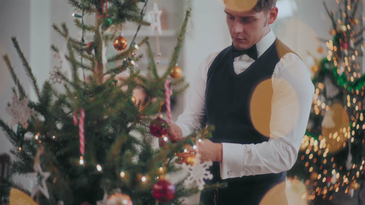 잘 옷을 입은 남자가 집에서 크리스마스 트리를 장식하고 있다