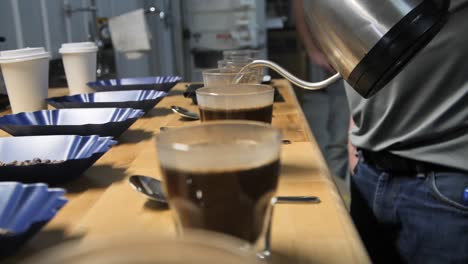 Man-pours-hot-water-for-coffee-cupping-taste-test,-slow-motion-close-up