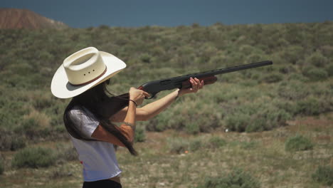 bonita chica caucásica disparando al plato en el desierto, dispara una escopeta de acción de bombeo con un fuerte retroceso