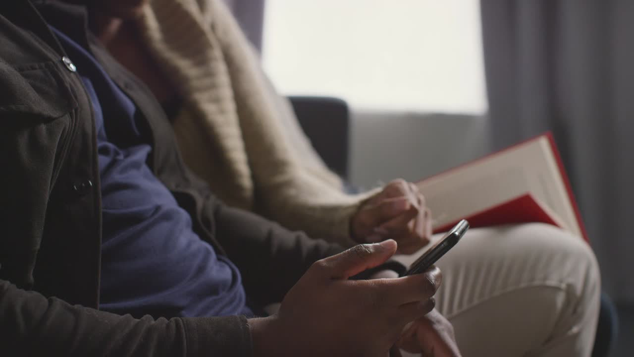 primer plano de una pareja en casa sentada en el sofá en la sala de estar discutiendo sobre lo que el hombre está mirando en el teléfono móvil