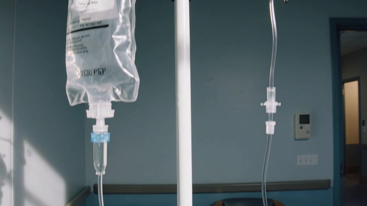 Ripresa dal basso che rivela un'asta portaflebo con sacca di fluido e tubicini in una stanza di degenza, documentazione delle cure