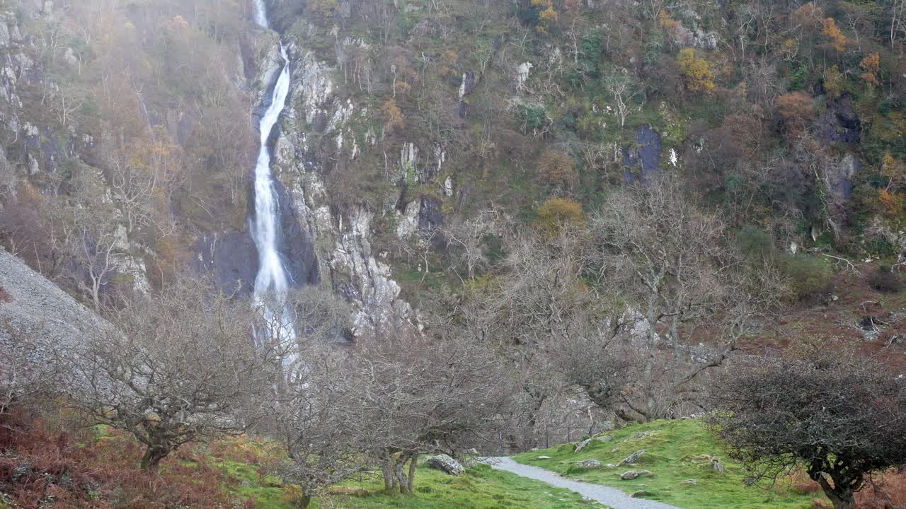 Trilha natural de outono levando a uma cachoeira em cascata através de árvores nuas e sem folhas.