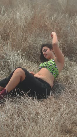 woman lying in dry grass, relaxed pose with hand behind head, calm outdoor vibe