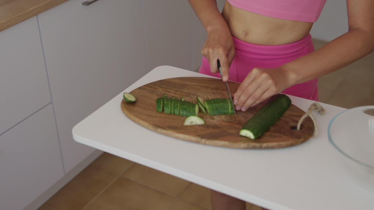 Woman cutting cucumber in kitchen