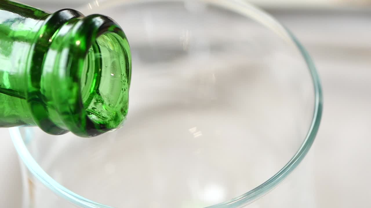 Pouring a drink into a glass from a green bottle
