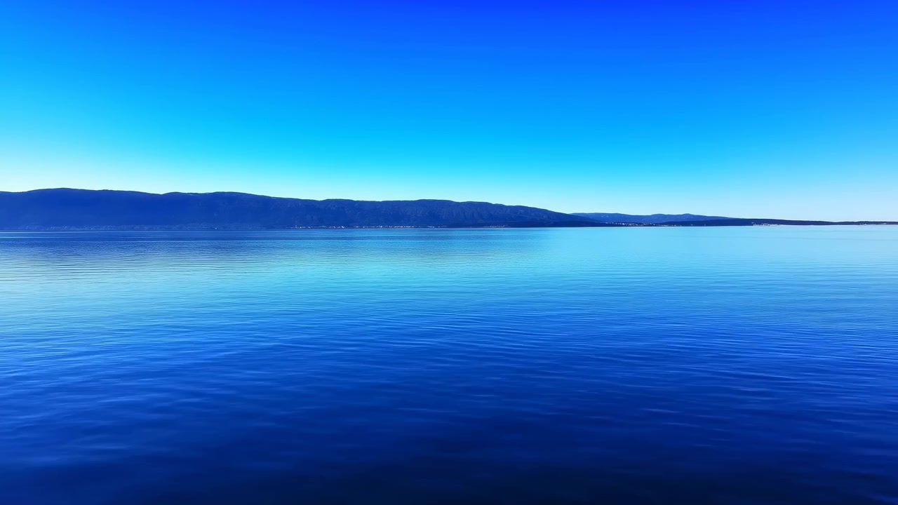 Kirkas sininen järvi vuorineen, peilimäinen vesi heijastaa harjannetta virheettömän taivaan alla, minimalistinen sommittelu.