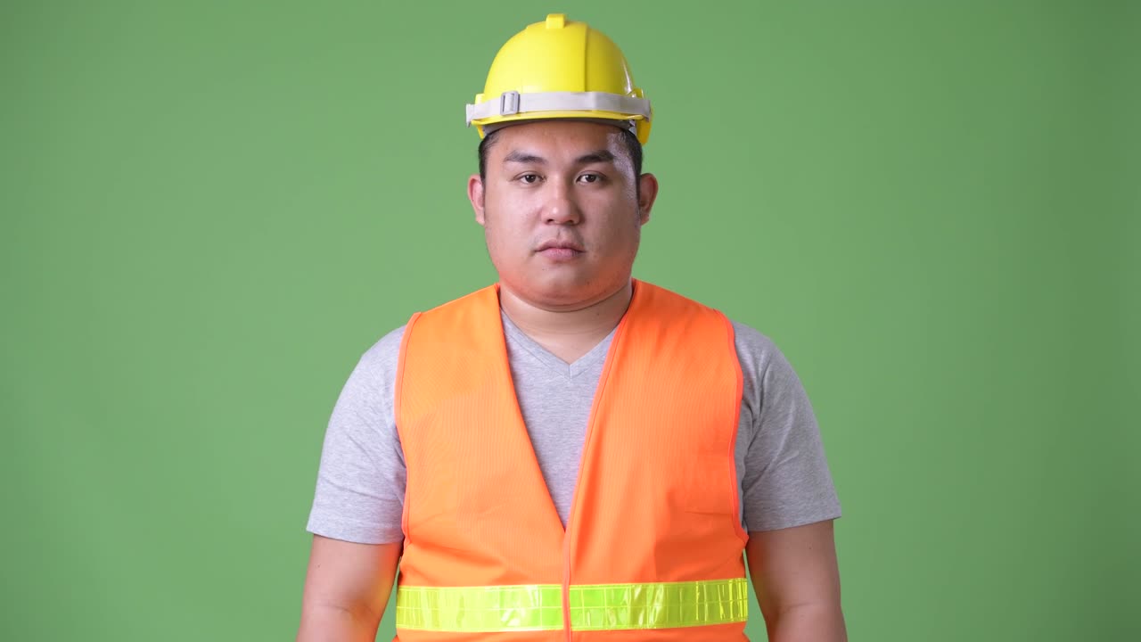 젊은 잘생긴 과체중 아시아인 남자 건설 노동자 초록색 배경