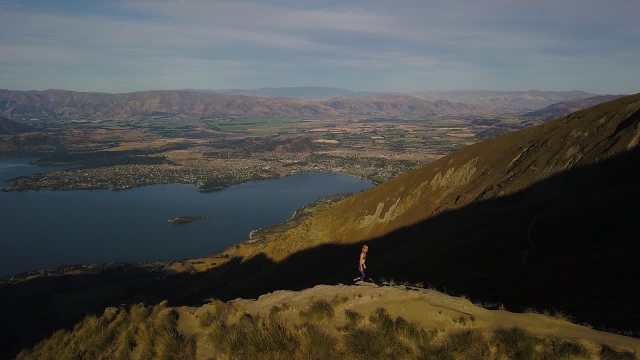una toma aérea orbital de barrido de una mujer atlética que disfruta de vistas espectaculares desde la cima de un famoso sendero de montaña